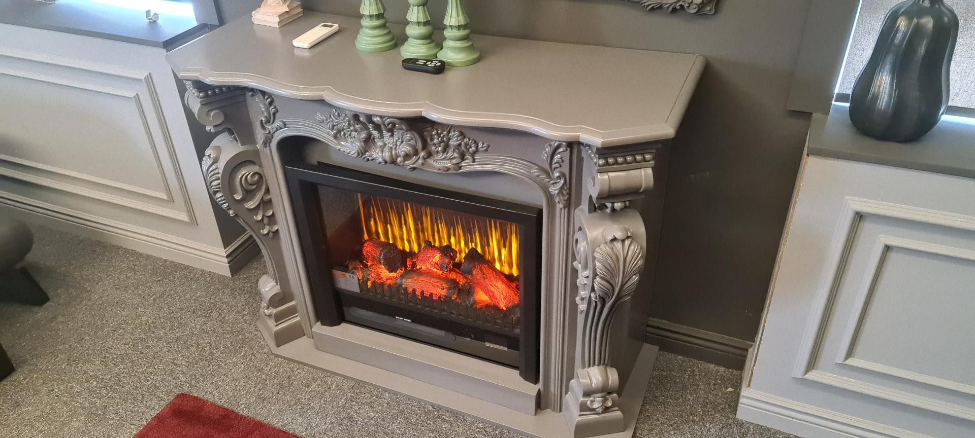 High angle view of a grey fireplace mantle console with serpentine shelf, floral frieze relief, and electric fire insert.