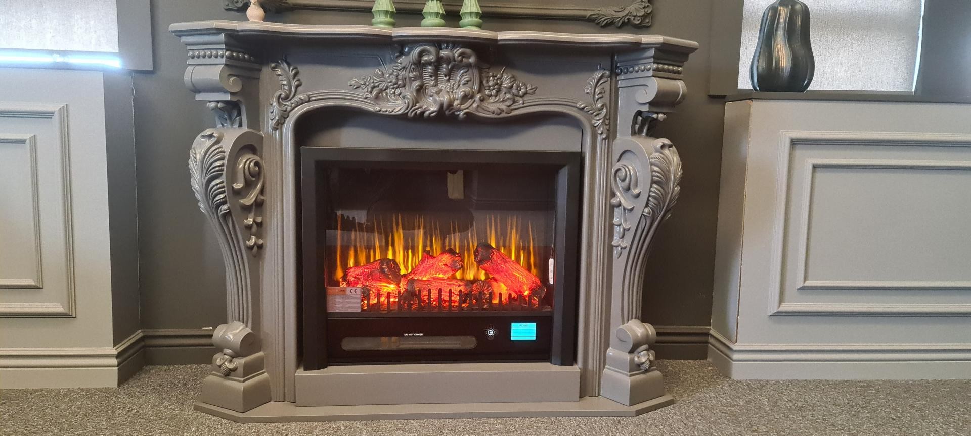 Front elevation of a grey carved polyurethane fireplace mantel centered between light grey wainscoting wall frames.