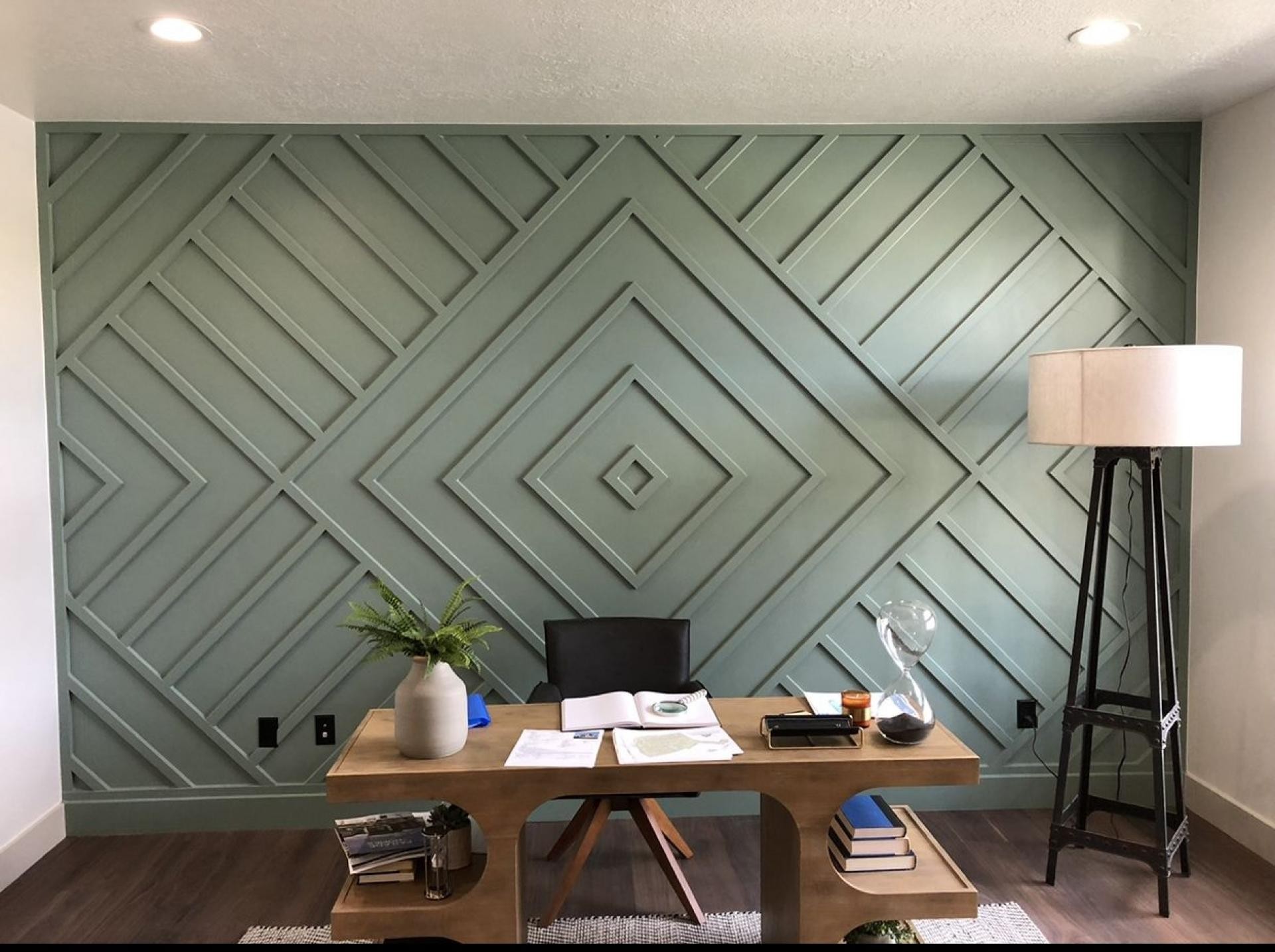 Sage green accent wall with a central concentric diamond pattern behind a wooden desk and office chair.