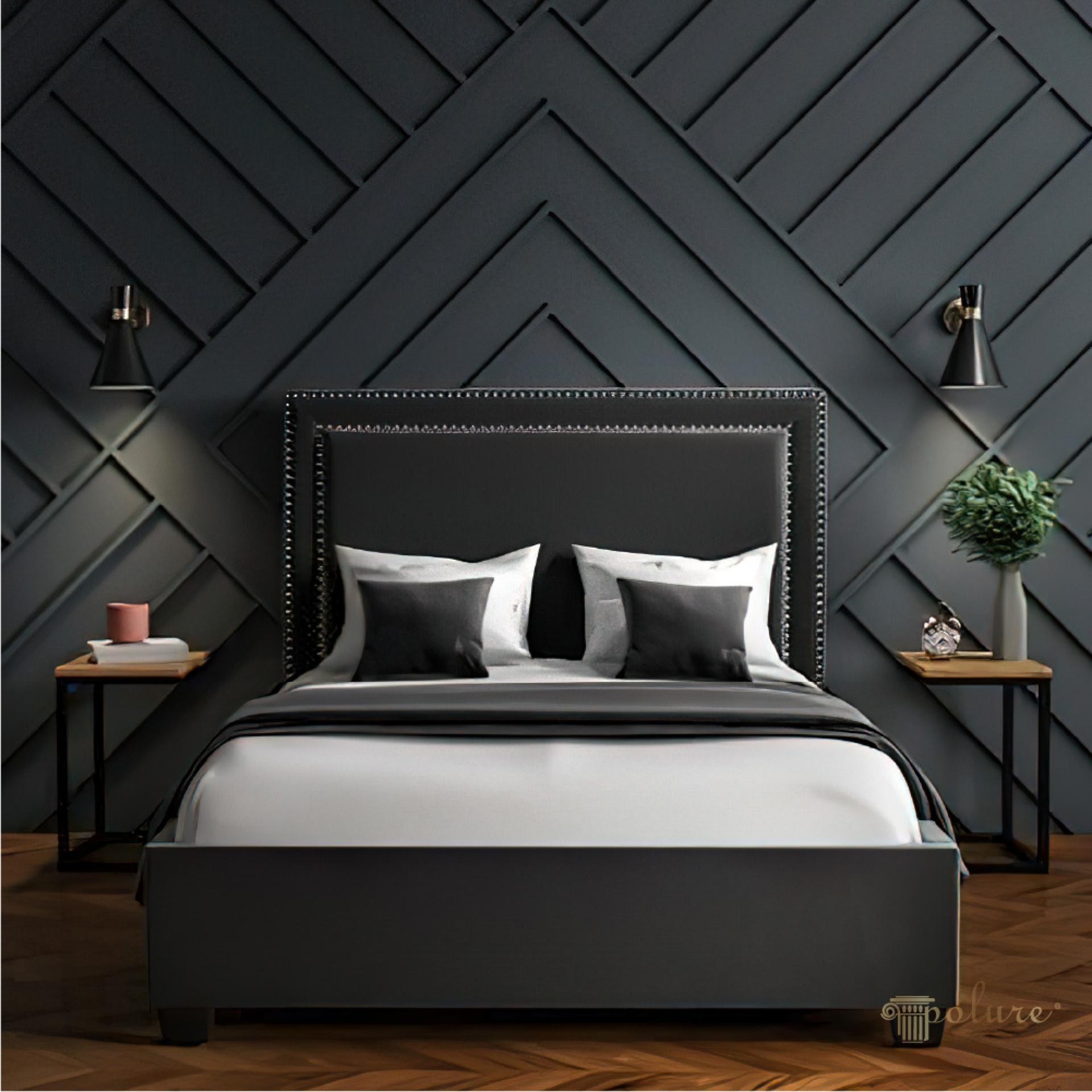 Dark charcoal chevron wall paneling with linear moulding strips behind a black nailhead upholstered bed.