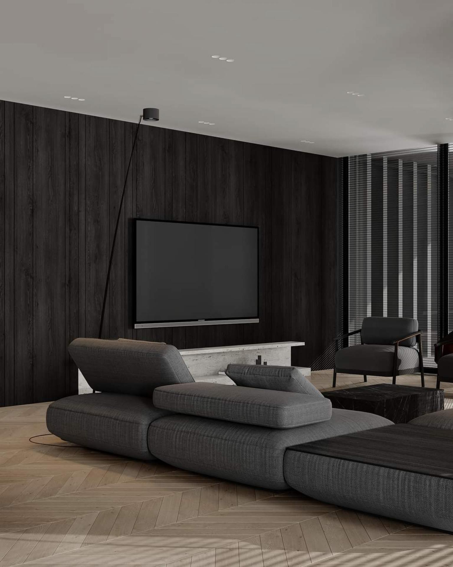 Modern living room with a dark charcoal wood paneled wall, a mounted flat-screen TV, grey modular low sofa, and light herringbone wood fl...