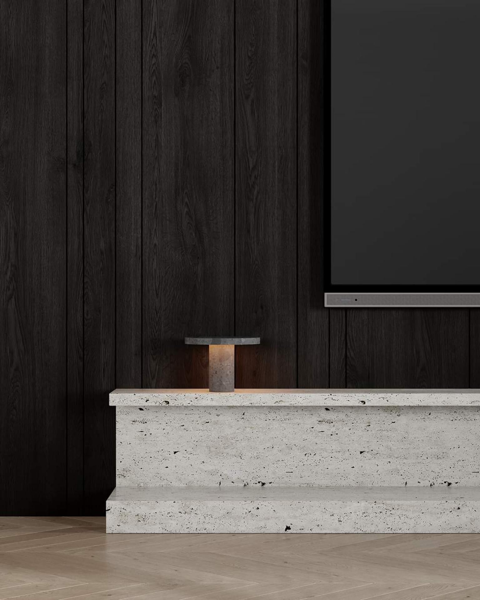 Close-up of a dark wood paneled wall, a travertine stone media console, a small glowing mushroom lamp, and a modern flat-screen TV.