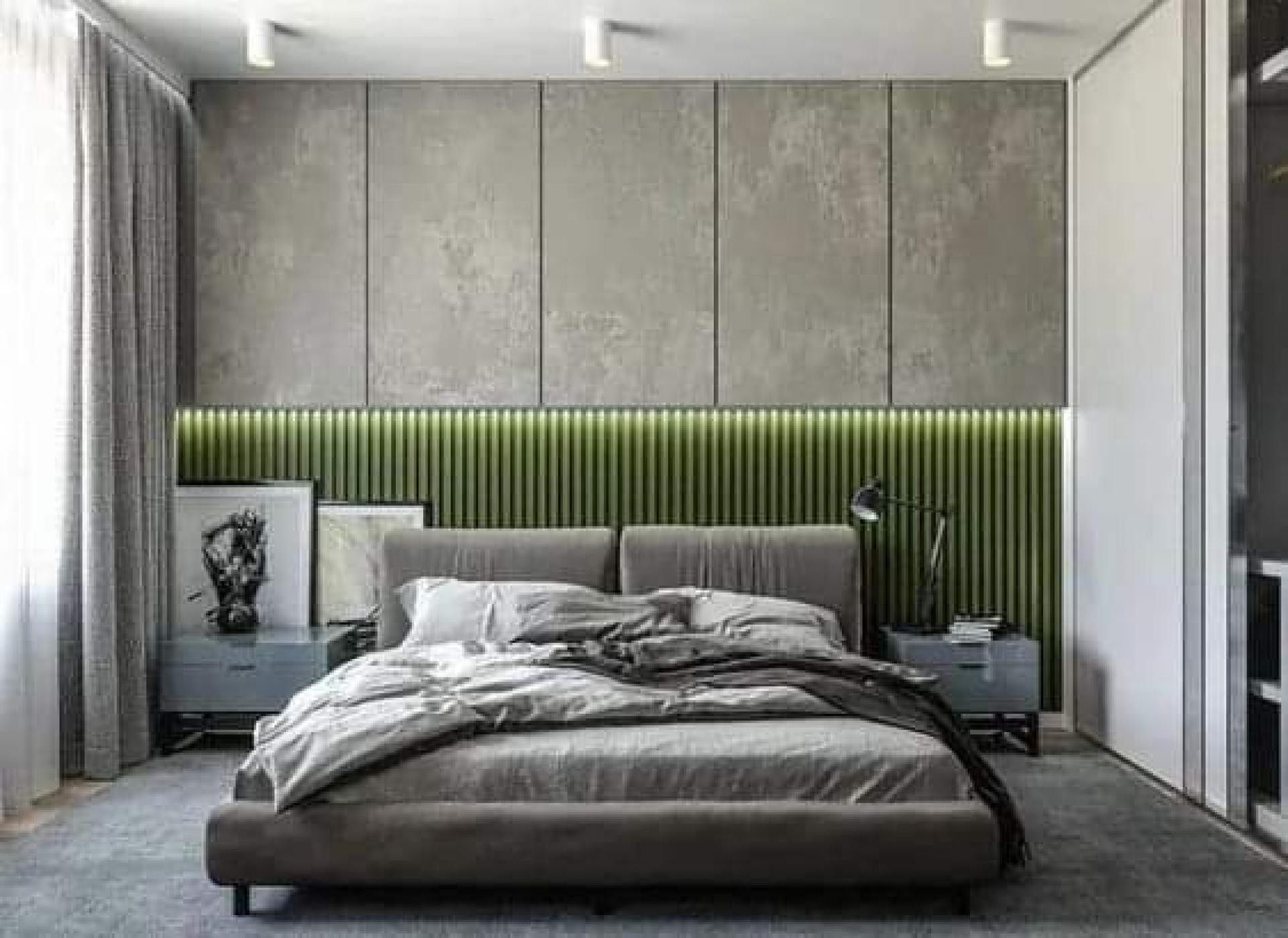Modern bedroom with a lower wall of green fluted panels, upper grey storage cabinets, hidden LED lighting, and a grey upholstered platfor...
