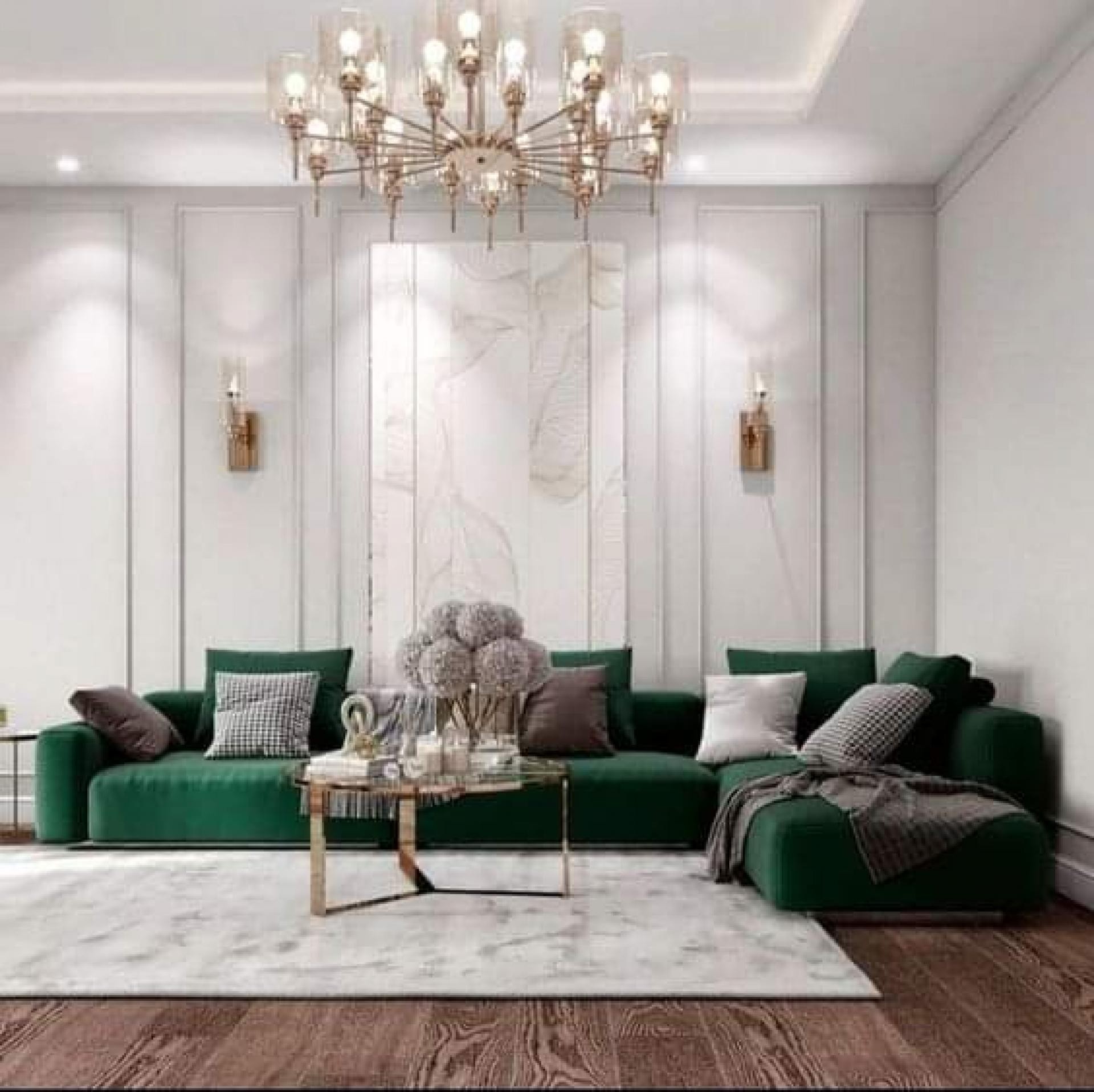 Bright white living room with tall rectangular wall moldings, a large emerald green velvet sectional sofa, and a multi-tiered brass chand...