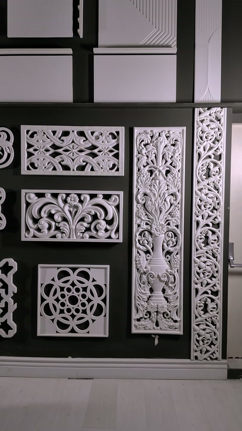 Geometrické a botanické reliéfne panely vypĺňajú čiernu prezentačnú stenu.