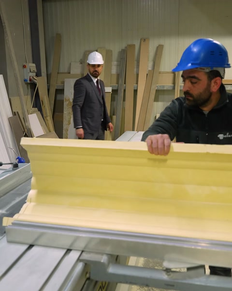 Un artesano inspecciona de cerca un perfil de cornisa de poliuretano amarillo en bruto