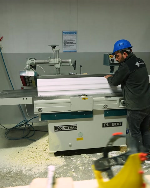 Trabajadores operan una sierra de precisión que corta un perfil de moldura de poliuretano