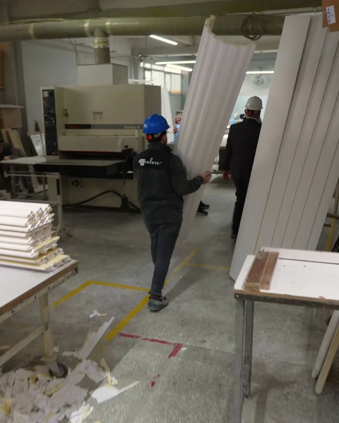 Un trabajador transporta perfiles de cornisa de poliuretano blanco terminados en el taller