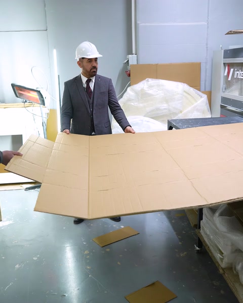 Un gerente transporta una gran lámina de cartón para embalaje en el taller