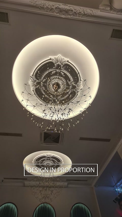 Un élément circulaire lumineux au plafond entoure un médaillon orné et un lustre.