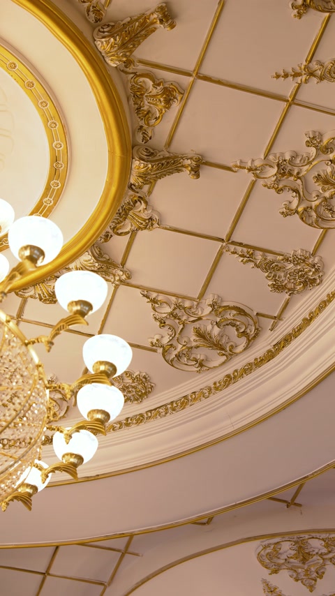 Geschwungene Gesimse und verzierte goldene Reliefs umgeben die Deckenleuchten