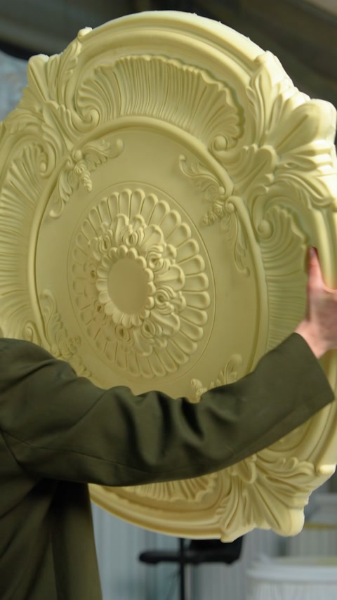 Ouvrier tenant un médaillon de plafond jaune non peint avant sa finition