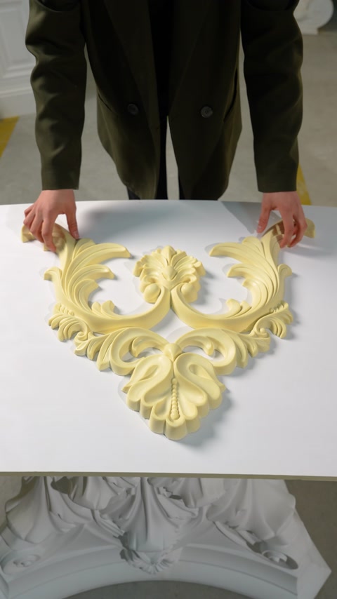 Mains assemblant des éléments d’ornement en volutes sculptées sur une table blanche