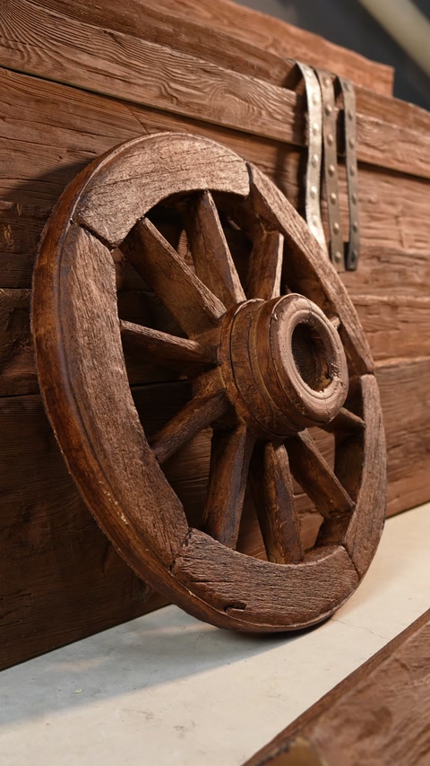 Roue de charrette en bois à côté d’une poutre rustique imitation bois