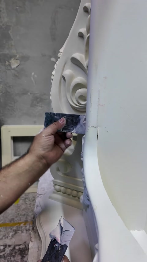 Řemeslník vyhlazuje spáru vedle spirálového ornamentu krbu.