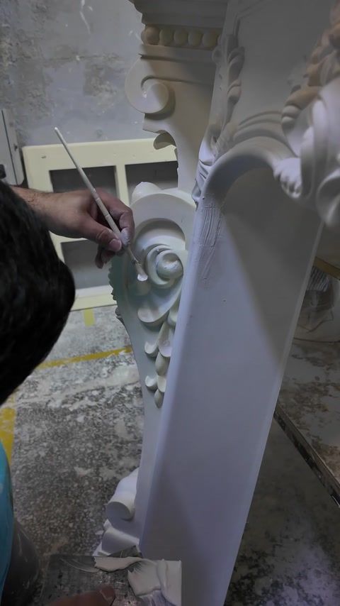 Jemná práce štětcem upravuje vyřezávaný spirálový ornament na dekorativní podpěře.