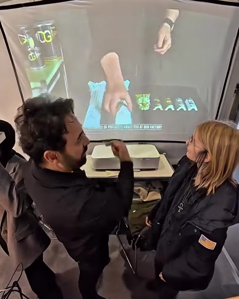 Muž předvádí VR brýle, zatímco žena sleduje virtuální ruku na obrazovce