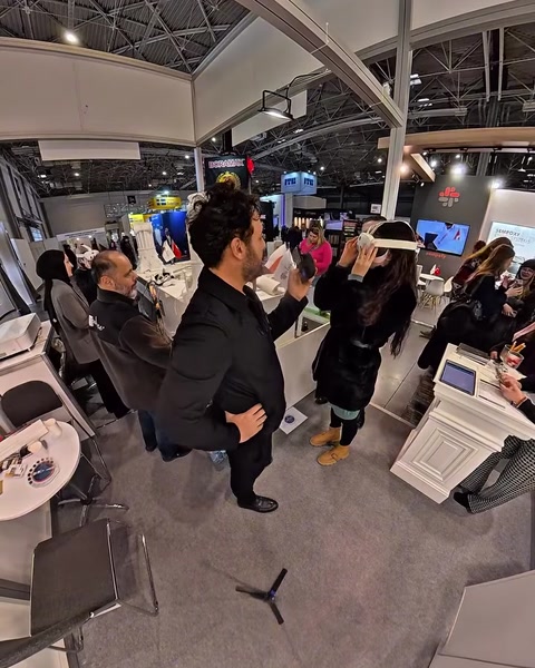 Muž s VR brýlemi gestikuluje, zatímco lidé sledují blízký monitor