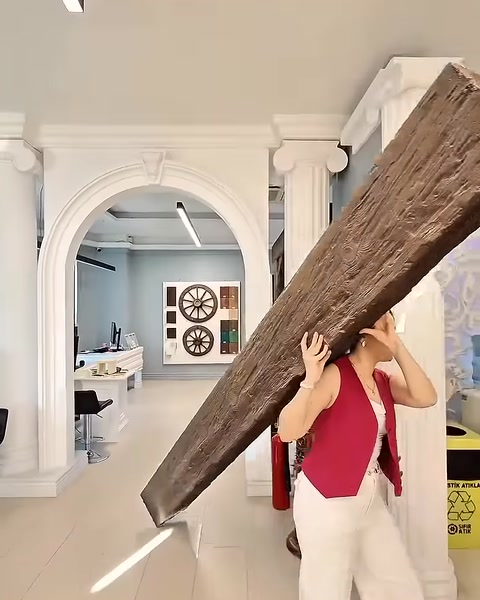 Woman carries lightweight beam past classical white pilasters and archway