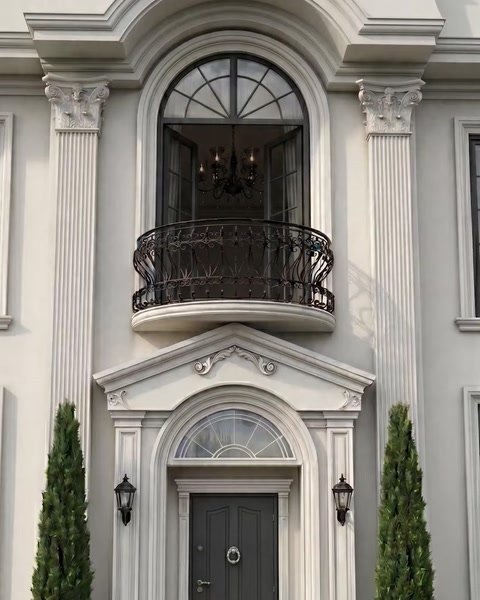 Ingresso di villa con alti pilastri, ringhiera del balcone e finestra ad arco