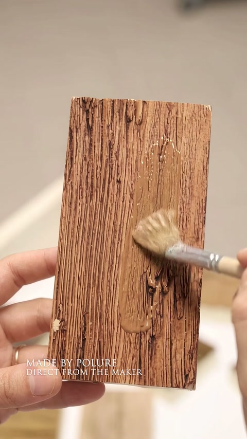 Un pinceau applique une finition brun chaud sur un échantillon texturé en polyuréthane.
