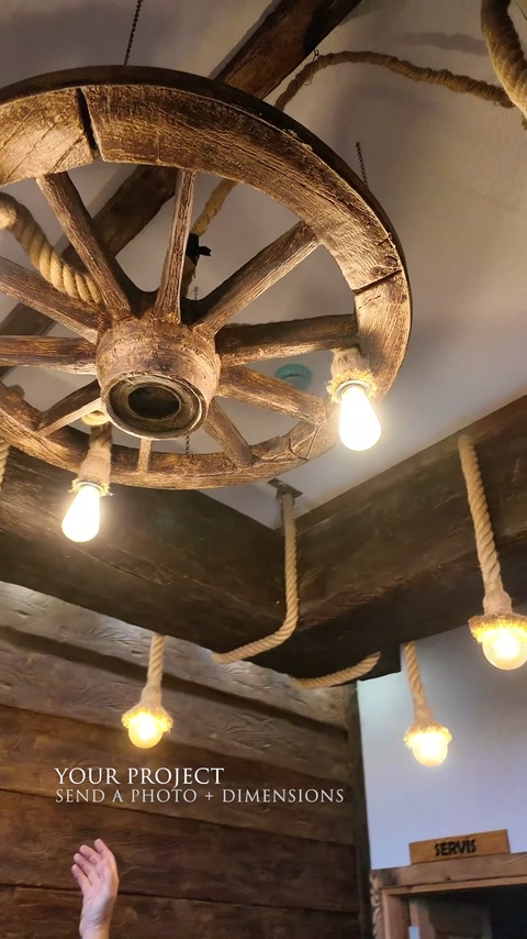 Un luminaire suspendu en roue de chariot complète des poutres imitation bois foncées dans un intérieur rustique.