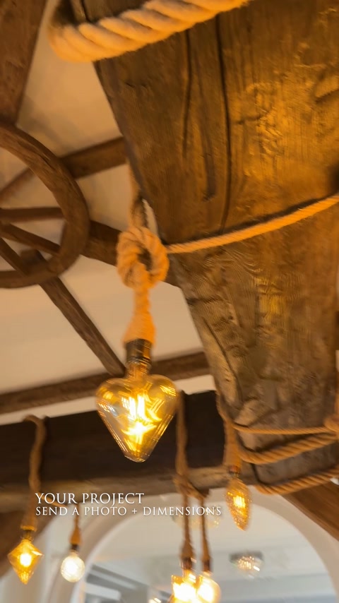 Un éclairage suspendu par des cordes se trouve sous de larges poutres de plafond rustiques.