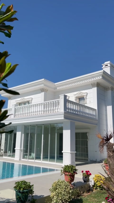 Die weiße Fassade kombiniert Balkonbaluster, Fensterumrahmungen und Dachgesimse.