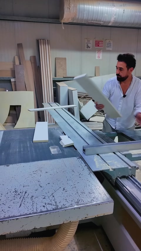 Een medewerker tilt een gezaagde kroonlijstlengte boven de zaagtafel