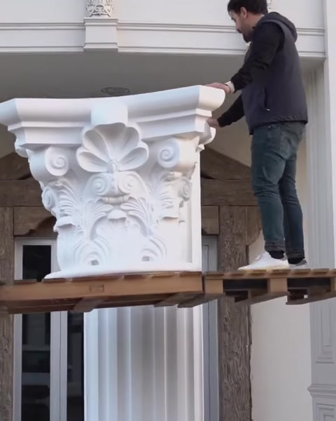 Arbeiter hebt korinthisches Kapitell auf erhöhte Plattform für Säule.