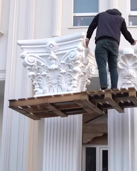 Arbeiter steht auf Plattform neben gehobenem Kapitell nahe Säule.