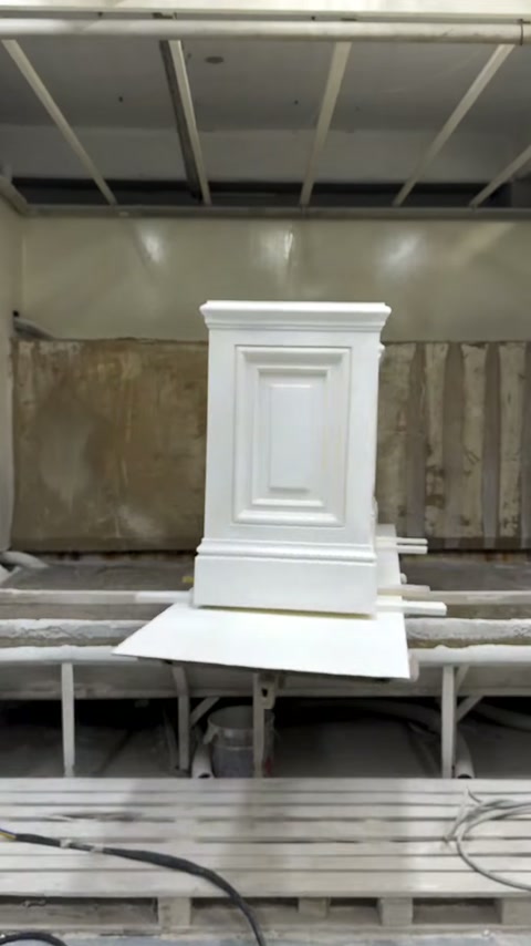 Un piédestal blanc à panneaux terminé repose dans la cabine de finition par pulvérisation.