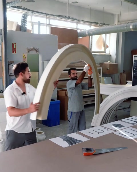 Two workers lifting a large white arch module inside the workshop