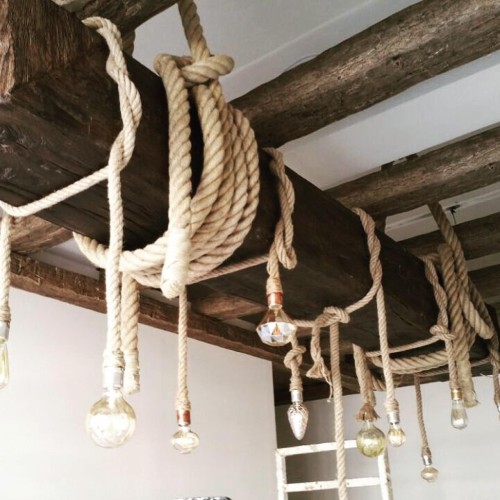 Travi rustiche in poliuretano con corde e lampade decorative <h2>Armonia tra rustico e classico</h2><p>Le travi in <strong>poliuretano</strong> offrono il fascino del legno antico senza i limiti del materiale naturale. La loro texture presenta venature scolpite che rievocano la robustezza storica delle travi portanti, ma in chiave più leggera e versatile. In questa composizione, le corde intrecciate si avvolgono intorno alle travi creando nodi decorativi che diventano non solo funzionali, ma anche un ornamento visivo.</p><p>L’uso delle <strong>corde</strong> introduce un richiamo alla tradizione marinaresca, in cui nodi e avvolgimenti rappresentavano sicurezza e solidità. Oggi questi dettagli rivivono come scelta estetica, rendendo il soffitto un elemento scenografico. Le lampade appese aggiungono un contrasto tra linee geometriche e forme organiche, in particolare grazie alle diverse tipologie di vetro e taglio delle lampadine.</p><h2>Geometrie e motivi decorativi</h2><p>Le linee parallele delle <strong>travi rustiche</strong> creano una scansione visiva che guida lo sguardo lungo tutta la stanza, mentre le corde disegnano traiettorie ondulate che spezzano la rigidità della composizione. I nodi a cappio e gli avvolgimenti regolari fungono da <strong>motivi decorativi</strong> che ricordano gli schemi geometrici della tradizione artigianale.</p><ul><li>Venature scolpite che imitano fedelmente il legno antico.</li><li>Nodi e avvolgimenti regolari delle corde.</li><li>Lampade decorative con forme geometriche differenti.</li></ul><p>Storicamente le travi in legno hanno rappresentato elementi costruttivi fondamentali fin dall’architettura romana, simbolo di robustezza e calore domestico. L’uso di varianti in poliuretano permette oggi di ricreare quell’atmosfera con maggiore flessibilità, senza rinunciare alla durata e alla resa estetica.</p><h2>Luce e atmosfera</h2><p>Le lampade sospese con bulbi trasparenti o sfaccettati creano giochi di riflessi che impreziosiscono la stanza. L’illuminazione diffusa e calda amplifica la sensazione di accoglienza, rendendo l’ambiente perfetto per chi cerca uno stile <strong>rustico-classico</strong> capace di combinare funzionalità ed eleganza.</p>
<p>Le travi in poliuretano con corde decorative rappresentano una soluzione originale per gli interni. Esse combinano la resistenza moderna con l’estetica del legno antico. Le corde intrecciate introducono un fascino artigianale particolare. I nodi ben definiti diventano elementi di design. Le lampade sospese diffondono luce calda ed elegante. Le diverse forme delle lampadine creano contrasti visivi. La texture delle travi riproduce fedelmente motivi naturali. Le geometrie lineari incontrano traiettorie morbide delle corde. Questo gioco di contrasti genera armonia negli spazi. Gli avvolgimenti regolari rafforzano l’effetto scenografico. La scelta dei materiali artificiali garantisce leggerezza. Le composizioni luminose evocano atmosfera intima. Lo stile rustico-classico si adatta facilmente a più contesti. Le corde e le travi diventano punti focali. L’insieme esprime un equilibrio tra tradizione e modernità.</p>