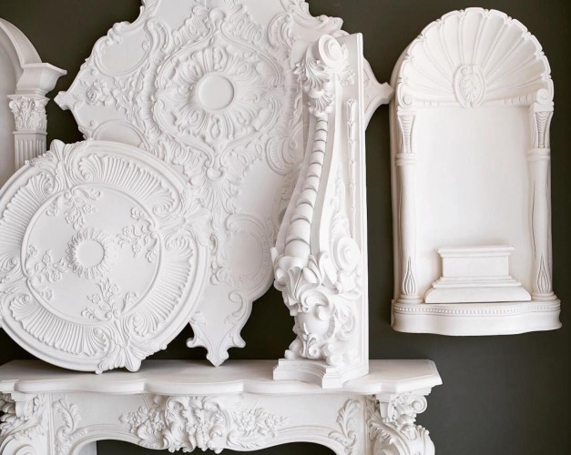 Decoración clásica en poliuretano con rosetones, cornisas y nichos ornamentales <h2>Detalles de la decoración clásica en poliuretano</h2><p>El uso de <strong>poliuretano</strong> en la decoración interior permite reproducir con precisión motivos tradicionalmente realizados en yeso o madera. En la imagen se observan <strong>rosetones</strong> con formas circulares y cuadrangulares, decorados con relieves florales y volutas que evocan la estética <strong>barroca</strong>.</p><p>También se destaca un <strong>nicho</strong> con forma de concha y una repisa central, ideal para enfatizar figuras decorativas o religiosas. La textura blanca aporta luminosidad y resalta los detalles de las molduras.</p><p>En la parte inferior se aprecia una consola con ornamentación floral y guirnaldas que recuerdan la tradición del <strong>rococó</strong> francés, caracterizada por su dinamismo y abundantes curvas. Este tipo de decoración tiene raíces en la arquitectura clásica, donde elementos como columnas y frisos se unían a rosetones y medallones en techos de salones palaciegos.</p><ul><li>Rosetones circulares y cuadrados con patrones simétricos.</li><li>Nicho en forma de concha con cornisa ornamentada.</li><li>Cornisas con hojas acanaladas y volutas en espiral.</li><li>Consola con relieves de flores y guirnaldas.</li></ul><p>Estas piezas de poliuretano son ligeras, fáciles de instalar y duraderas, logrando un aspecto clásico refinado en ambientes modernos.</p>
<p>El uso de <strong>poliuretano</strong> en decoración transforma los interiores en espacios elegantes y atemporales. Los <strong>rosetones</strong> circulares muestran relieves florales que crean simetría visual. Las cornisas con volutas añaden un aire ceremonial a las paredes. El <strong>nicho</strong> con forma de concha resalta la tradición ornamental clásica. La textura blanca intensifica el detalle de cada motivo tallado. El estilo <strong>barroco</strong> se refleja en la abundancia de curvas y flores. El rococó aporta dinamismo en cada composición. Los patrones geométricos guían la vista hacia el centro. Los relieves de guirnaldas evocan una ornamentación delicada. La ligereza del material facilita su instalación. La durabilidad asegura que los detalles perduren. Su versatilidad lo hace apto para hogares y espacios públicos. Evoca la grandeza de los salones palaciegos. Permite personalizar techos y paredes con precisión. Crea un equilibrio entre modernidad y clasicismo.</p>