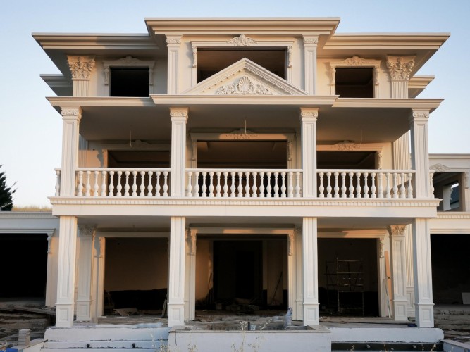 Klassische Villa mit Poliurethan-Fassade und detailreichen Holzoptik-Elementen <h2>Klassische Eleganz in moderner Umsetzung</h2><p>Die Fassade dieser Villa vereint klassische Architekturformen mit innovativen <strong>Poliurethan</strong>-Elementen, die eine realistische <strong>Holzoptik</strong> erzeugen. Durch diese Technik wird ein natürlicher und zugleich pflegeleichter Charakter erreicht.</p><p>Markant sind die hohen Säulen mit reich dekorierten Kapitellen im korinthischen Stil, die an antike Vorbilder erinnern. Auch die <strong>Balustraden</strong> und das dreieckige <strong>Giebelfeld</strong> mit filigranen Rankenmustern verleihen der Architektur eine ausgewogene, kunstvolle Wirkung.</p><p>Die klaren horizontalen Gesimse strukturieren die Fassade in Ebenen und betonen die klassische Symmetrie. Geschwungene ornamente und präzise gearbeitete Reliefs setzen feine Akzente, ohne die monumentale Gesamtwirkung zu verlieren.</p><p>Historisch gesehen finden sich ähnliche Formgebungen in römischen Villen und Renaissancebauten, wo die Harmonie zwischen Funktionalität und dekorativer Ästhetik im Mittelpunkt stand. Diese moderne Ausführung greift diese Traditionen auf und interpretiert sie zeitgemäß.</p><ul><li>Elegante Säulen mit Kapitellen</li><li>Kunstvolle Balustraden</li><li>Ornamentreiche Gesimse und Giebelformen</li><li>Poliurethan mit Holzoptik für warme Wirkung</li></ul>
<p>Diese Villa zeigt klassische Schönheit und starke Symmetrie. Sie wirkt durch filigrane Details sehr edel. Die Kombination aus modernen Materialien und historischen Formen überzeugt. Besonders auffällig sind die kraftvollen Säulen. Das Ornament im Giebelfeld ist ein Blickfang. Auch die kunstvoll gearbeiteten Balustraden fallen sofort ins Auge. Die Fassade lebt von klarer Ordnung und viel Harmonie. Poliurethan sorgt für Leichtigkeit und Beständigkeit. Gleichzeitig wirkt die Holzoptik warm und einladend. Reliefs und feine Muster betonen die Handwerkskunst. <strong>Säulen</strong>, <strong>Balustraden</strong> und <strong>Gesimse</strong> verleihen Eleganz. Die Villa kombiniert antike Inspiration mit moderner Technik. Ihr Erscheinungsbild ist ausdrucksstark und monumental. Die Oberflächen reflektieren das Licht angenehm. Insgesamt entsteht ein zeitloser Charakter mit erlesener Raffinesse.</p>