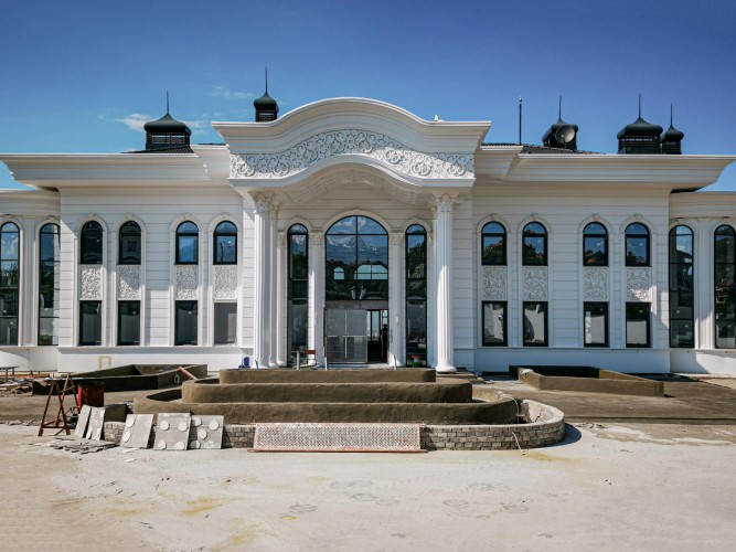 Decoração clássica com poliuretano para fachadas de villas e palácios <h2>Ornamentação clássica em poliuretano</h2><p>A fachada em estilo clássico exibe colunas inspiradas no modelo coríntio, frontão curvilíneo e painéis decorativos aplicados em alto-relevo. O uso do <strong>poliuretano</strong> permite criar arabescos, rendilhados e molduras com precisão, reforçando a sensação de sofisticação e imponência.</p><p>Entre os destaques estão os arcos de janelas alongados, as <strong>colunas</strong> brancas robustas e o friso contínuo que percorre a extensão do edifício. Esse equilíbrio entre simetria e ornamentação remete a influências históricas do período renascentista e barroco, quando a composição detalhada era utilizada para evidenciar prestígio e poder.</p><p>No conjunto, a integração de <strong>motivos geométricos</strong> e relevos florais garante um efeito rico em luz e sombra, ressaltando o caráter cenográfico da construção. Além disso, os elementos curvilíneos do frontão, em contraste com as linhas horizontais do corpo central, acrescentam dinamismo visual.</p><p>O <strong>design clássico</strong> aliado ao material moderno proporciona durabilidade e leveza estrutural, permitindo que grandes formas decorativas sejam aplicadas sem sobrecarregar a fachada. Esse tipo de solução é ideal para <strong>fachadas</strong> de villas, yalis e palácios que buscam manter uma identidade imponente.</p><ul><li>Colunas ornamentadas com capitéis detalhados</li><li>Arcos altos que reforçam verticalidade</li><li>Painéis decorativos com rendilhado em poliuretano</li><li>Frontão curvo com arabescos clássicos</li></ul>

<p>A fachada em estilo clássico destaca-se pelo uso de <strong>poliuretano</strong> em detalhes ornamentais. Os arcos altos criam verticalidade e harmonia visual. As <strong>colunas</strong> brancas reforçam o caráter histórico e imponente. O frontão curvo com arabescos traz movimento à composição. Os painéis em relevo adicionam textura e sofisticação. A integração de <strong>motivos geométricos</strong> e florais garante equilíbrio estético. A simetria estrutural dá coesão ao conjunto arquitetônico. O material escolhido assegura durabilidade em ambientes externos. O acabamento leve possibilita formas complexas sem sobrecarga. O <strong>design clássico</strong> conecta tradição e modernidade. O uso de frisos contínuos reforça linearidade. A combinação de elementos históricos remete à arquitetura palaciana. A escolha estética valoriza propriedades exclusivas. O uso de poliuretano cria riqueza visual e detalhamento. Essa abordagem traduz luxo e elegância em fachadas contemporâneas.</p>