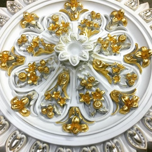 Roseta clássica de poliuretano com detalhes em dourado e motivo floral <h2>Roseta Clássica de Poliuretano</h2><p>Este modelo de roseta foi criado em <strong>poliuretano</strong>, um material resistente e leve, que permite riqueza de detalhes no design ornamental. Sua composição mistura forma circular com motivos quase radiais, distribuídos de forma equilibrada.</p><p>A peça apresenta <strong>detalhes dourados</strong> em pintura que ressaltam delicadamente cada elemento floral em alto-relevo, especialmente pequenos ramos, flores e frutos. A combinação do tom branco com o dourado cria um contraste sofisticado que se adapta a <strong>decoração clássica</strong> de interiores.</p><p>Entre os destaques artísticos encontram-se ornamentos que lembram <strong>motivos florais</strong> da tradição europeia, com pétalas, brotos e folhas dispostos em forma simétrica, reforçando a sensação de ordem estética e elegância monumental.</p><p>No contexto histórico, ornamentos desse tipo já eram comuns em tetos de mansões e palácios renascentistas, assim como em vilas do período barroco, onde o relevo florido e metálico acentuava a iluminação dos ambientes.</p><ul><li>Material durável e de fácil instalação;</li><li>Acabamento refinado com pintura dourada;</li><li>Design versátil que valoriza tetos de ambientes sofisticados.</li></ul><p>É ideal para ambientes que buscam um ar nobre e artístico, sobretudo em projetos personalizados de vilas clássicas e decorações luxuosas.</p>

<p>Esta roseta de poliuretano com <strong>detalhes dourados</strong> destaca-se pela harmonia entre simetria e delicadeza. Seu relevo com <strong>motivos florais</strong> inspira elegância em qualquer espaço clássico. A peça conversa com tradições históricas de ornamentação usada em palácios e mansões. O material leve facilita a instalação sem perder sofisticação. O contraste entre branco e dourado traz profundidade. A simetria radial cria sensação de equilíbrio decorativo. O relevo detalhado evidencia flores e folhas em composição requintada. Sua forma central em círculo acentua a estética harmônica. Esta roseta valoriza amplos salões ou vilas elegantes. O estilo clássico proporciona atemporalidade e nobreza. A riqueza ornamental em dourado captura a luz com efeito refinado. O acabamento revela excelência artesanal. O design único se adapta a variadas propostas de decoração. É um elemento versátil que une tradição e inovação. A roseta em <strong>poliuretano</strong> é ideal para quem busca luxo e durabilidade.</p>