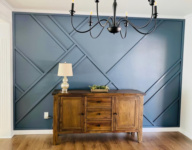 Pared de acento azul con moldura poliuretano asimétrica estilo moderno clásico <h2>Pared de acento con moldura asimétrica</h2><p>La combinación de <strong>molduras de poliuretano</strong> y un tono azul intenso establece un estilo <strong>moderno clásico</strong> que da protagonismo a la pared principal de la estancia. Las líneas cruzadas en ángulos diagonales generan un patrón <strong>geométrico</strong> dinámico, aportando movimiento sin perder elegancia.</p><p>Los listones enmarcan figuras irregulares que evocan la abstracción moderna, mientras la materialidad robusta recuerda la tradición de las boiseries clásicas. Este recurso tiene su origen en prácticas decorativas históricas, como los panelados geométricos del siglo XVIII, reinterpretados ahora en clave contemporánea.</p><h2>Composición visual y mobiliario</h2><p>El mobiliario de <strong>madera</strong> cálida destaca frente al azul profundo de la pared, generando contraste armónico. La lámpara de mesa clara suaviza la composición y la lámpara colgante negra de brazos curvos aporta equilibrio entre lo tradicional y lo actual.</p><ul><li>Geometría diagonal y audaz</li><li>Contraste entre azul frío y madera cálida</li><li>Inspiración moderna y clásica</li><li>Moldura durable y versátil</li></ul><p>Este concepto de diseño realza comedores y salones, añadiendo sofisticación con pocos elementos y gran impacto visual.</p>
<p>Una pared con molduras diagonales transmite energía a cualquier habitación. El uso del poliuretano permite un diseño resistente y ligero. La composición crea una estética moderna y equilibrada. El tono azul profundo refuerza la sensación de serenidad. El mobiliario de madera aporta calidez al conjunto decorativo. La lámpara negra añade un matiz clásico contemporáneo. La disposición diagonal de las líneas ofrece dinamismo visual. Los ángulos irregulares enriquecen el espacio con sofisticación. El contraste de tonos resalta el diseño general. La historia de los panelados geométricos inspira este enfoque. El estilo combina tradición y modernidad en armonía. El acabado invita a personalizar el espacio con estilo. El uso de <strong>geometría</strong> es clave en la propuesta. La textura del <strong>poliuretano</strong> eleva el carácter decorativo. Este equilibrio genera un ambiente <strong>moderno clásico</strong> único.</p>