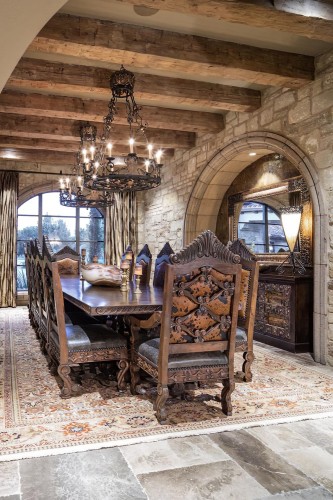 Salone classico rustico con travi in poliuretano e dettagli intagliati <h2>Travi in poliuretano e atmosfera rustico-classica</h2><p>Le travi in <strong>poliuretano</strong> che attraversano il soffitto esaltano il carattere rustico del salone, richiamando la solidità delle antiche case di campagna. La scelta del poliuretano permette di ottenere l’effetto estetico del legno massello senza appesantire la struttura.</p><p>Il grande tavolo centrale è circondato da sedie riccamente decorate con intagli complessi che raffigurano <strong>motivi floreali</strong> e <strong>geometrici</strong>. Questi dettagli artigianali richiamano la tradizione classica e nobilitano l’ambiente con un senso di pregio e durata.</p><h2>Decorazioni e giochi di luce</h2><p>I lampadari in <strong>ferro battuto</strong> con forme circolari e volute ornamentali portano un’illuminazione calda e diffusa. Essi ricordano le atmosfere medievali e si integrano perfettamente con gli archi in pietra e le grandi finestre che filtrano la luce naturale.</p><p>Lo specchio incastonato in una cornice scolpita amplifica la percezione dello spazio e valorizza i giochi luminosi. Le tende pesanti aggiungono un tocco di intimità e continuità con i toni dorati della stanza.</p><h2>Tappeti e pavimentazione</h2><p>Il tappeto persiano mette in risalto il pavimento in pietra naturale, creando un contrasto di texture che dona profondità. I suoi **motivi ornamentali** e la palette di colori caldi armonizzano la sala con elementi di cultura storica, richiamando modelli artistici ampiamente usati a partire dall’antichità classica.</p><p>Questa combinazione di elementi rustici e classici mostra come materiali diversi come pietra, ferro, poliuretano e tessuti possano fondersi in un ambiente equilibrato e accogliente.</p>

<p>Il soffitto con travi in <strong>poliuretano</strong> regala l’atmosfera calda del legno antico. Le pareti in pietra rafforzano l’impronta rustica della sala. Il grande tavolo in legno massiccio diventa il cuore conviviale dell’ambiente. Le sedie intagliate con <strong>motivi floreali</strong> e <strong>geometrici</strong> raccontano l’arte artigianale classica. I lampadari in ferro battuto diffondono una luce suggestiva. Le forme circolari delle strutture luminose dialogano con gli archi in pietra. Le tende spesse intensificano l’intimità dello spazio. Lo specchio con cornice decorata amplia la profondità visiva. Il tappeto persiano con disegni complessi armonizza i toni caldi. La pavimentazione in pietra naturale sostiene un carattere solido e duraturo. Le nuance dorate delle superfici danno eleganza al contesto. Tutti gli elementi sono bilanciati con coerenza estetica. Il contrasto di materiali crea ricchezza visiva. L’insieme rappresenta un equilibrio tra rusticità ed eleganza storica. Questo ambiente dimostra come dettagli minuziosi possano trasformare un salone in un luogo accogliente e raffinato.</p>