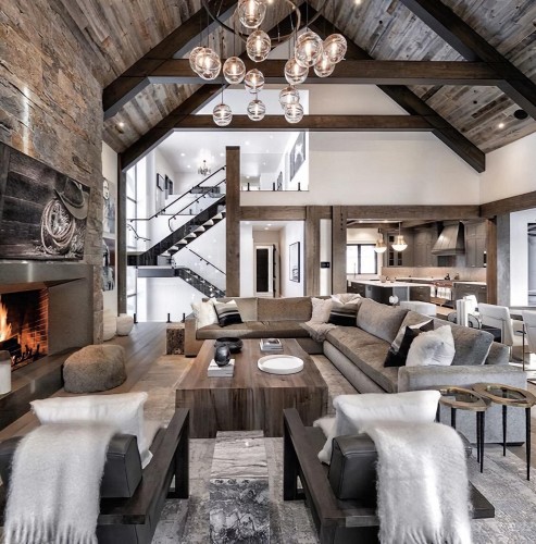 Rustik klassisches Wohnzimmer mit Holzdetails und zeitloser Eleganz <h2>Rustik und klassisch vereint</h2><p>Dieses Wohnzimmer präsentiert ein harmonisches Spiel aus <strong>Holz</strong>, Stein und Stoff. Die offene Architektur mit sichtbaren Balken und hohen Decken betont Großzügigkeit und Tiefe. Die Steinwand rund um den Kamin bringt eine handwerkliche Anmutung, während das knisternde Feuer gemütliche Wärme ausstrahlt.</p><p>Die dekorativen Elemente setzen auf geometrische Klarheit: rechteckige Linien im Couchtisch und die symmetrische Anordnung der Sofas lenken den Blick in die Mitte des Raumes. Im Gegensatz dazu wirken die runden Glasleuchten als leichter Kontrapunkt, der für ein modernes Gleichgewicht sorgt.</p><h2>Materialien und Details</h2><p>Besonders wirkungsvoll sind die dunklen Holzbalken an der Decke, die mit strukturierten Holzpaneelen eine rustikale Ausstrahlung erzeugen. Die Oberflächen zeigen bewusst die Maserungen und schaffen einen Bezug zur handwerklichen Tradition. Dekorative Schichtungen von Textilien auf Sofas und Sesseln, kombiniert mit neutralen Grautönen, geben dem Raum eine sanfte Eleganz.</p><p>Die lange Tradition von Steinelementen in Innenräumen geht bis in die klassische Architektur zurück, wo rau gearbeiteter Naturstein Stärke und Stabilität verkörperte. In diesem Raum wird dieser Gedanke neu interpretiert, indem die Steinwand mit modernem Interieur verschmilzt.</p><h2>Gesamtwirkung</h2><p>Das Ergebnis ist ein Interieur, das rustikale Ursprünglichkeit mit klassischer Eleganz und moderner Klarheit verbindet. Der Raum wirkt sowohl gemütlich als auch repräsentativ, ideal für gesellige Abende oder ruhige Momente.</p>

<p>Dieses Wohnzimmer vereint rustikale und klassische Gestaltung in einer ausgewogenen Atmosphäre. Sichtbare <strong>Holzbalken</strong> betonen die Höhe und schaffen Struktur. Der große Kamin mit <strong>Steinwand</strong> vermittelt Wärme und handwerkliche Stärke. Großzügige Sofas in neutralen Farben sorgen für Komfort. Runde Glasleuchten bringen Leichtigkeit in die Decke. Natürliche Texturen verstärken den rustikalen Charakter. Ein massiver Holztisch bildet das Zentrum der Raumgestaltung. Die Anordnung der Möbel fördert Geselligkeit. Sanfte Teppichmuster mit geometrischen Elementen erzeugen Balance. Ein offener Raumfluss verbindet Wohnbereich und Küche elegant. Klassische Details treffen auf moderne Geradlinigkeit. Die Materialien schaffen eine authentische Wohnlichkeit. Stein, Holz und Stoff wirken harmonisch zusammen. Der Stil wirkt zeitlos und doch modern. So entsteht ein rustik klassisches Zuhause mit einzigartigem Charme.</p>