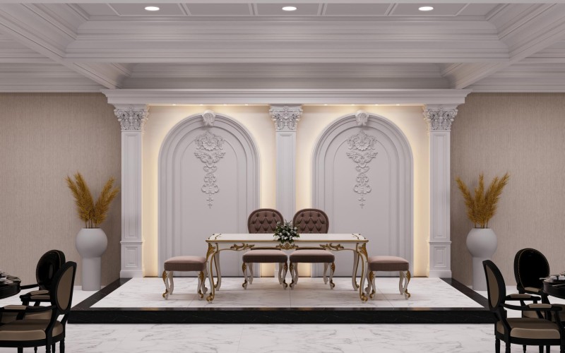 Decoração clássica de salão de casamentos com colunas de poliuretano e detalhes ornamentais <h2>Decoração clássica com colunas de poliuretano</h2><p>O palco foi projetado com <strong>colunas de poliuretano</strong> em estilo clássico, trazendo imponência e harmonia visual. Os arcos emoldurados com ornamentos florais formam o pano de fundo e criam profundidade. A iluminação embutida realça os detalhes do relevo e proporciona uma atmosfera acolhedora ao espaço.</p><p>A mesa nupcial central se destaca com acabamento branco, arabescos dourados e cadeiras estofadas em capitonê que completam a composição. O piso em mármore claro com molduras escuras reforça a sensação de sofisticação. No entorno, vasos de cerâmica com arranjos secos dão contraste natural ao conjunto. O teto decorado em linhas geométricas cria equilíbrio arquitetônico e conduz o olhar ao cenário principal.</p><p>As decorações foram inspiradas em estilos gregos e romanos, lembrando elementos de ordem <strong>coríntia</strong> com folhas esculpidas nos capitéis das colunas. Esse detalhe conecta a concepção atual a um passado histórico, trazendo autenticidade e refinamento. O projeto combina tradição e modernidade, integrando <strong>design clássico</strong> com <strong>materiais modernos</strong>.</p><ul><li>Detalhes ornamentais em alto-relevo.</li><li>Paleta de cores neutras com dourado sofisticado.</li><li>Integração de elementos históricos e contemporâneos.</li></ul>

<p>A decoração deste salão de casamentos aposta em <strong>colunas de poliuretano</strong> que trazem imponência ao palco. Os arcos ornamentados oferecem um cenário clássico bem equilibrado. O uso de acabamentos dourados adiciona contraste refinado. As cadeiras capitonê reforçam a elegância. O mármore claro do piso transmite uma sensação de luxo. Os vasos de cerâmica equilibram a composição com naturalidade. A iluminação suave destaca ornamentos detalhados. O teto ripado cria continuidade visual. O estilo <strong>coríntio</strong> inspira a ornamentação superior. Os relevos florais criam autenticidade clássica. O conjunto adapta tradição a novos materiais. O design prioriza a harmonia e o conforto. A atmosfera é sofisticada e acolhedora. O <strong>design clássico</strong> integra bem com toques modernos. A proposta resulta em um espaço memorável para casamentos.</p>