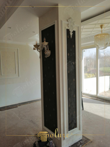 Polyurethaan wandpanelen met klassieke details voor elegante woonkamerdecoratie <h2>Klassieke elegantie met polyurethaan wandpanelen</h2><p>De getoonde salonwand combineert <strong>polyurethaan</strong> lijsten met een donkere achtergrond waarin subtiele motieven zijn verwerkt. Deze symmetrische structuur legt de nadruk op klassieke <strong>geometrie</strong> en versterkt het gevoel van balans en duurzamiteit.</p><p>Decoratieve details zoals een wandarmatuur in antieke stijl en een ornament boven de lijst zorgen voor <strong>stijlvol</strong> karakter. De donkere bekleding met fijne patronen contrasteert met het witte kader en benadrukt de verticale lijnen van de wand.</p><p>Het spel van rechthoeken en dieptewerking geeft de ruimte een <strong>architectonisch</strong> accent. Dit soort elementen hebben hun oorsprong in historische interieurs, geïnspireerd door klassieke Griekse en Romeinse stijlen waar kolommen en ornamentieke elementen een centrale rol speelden.</p><p>De combinatie van neutraal wit en donker textielachtig oppervlak maakt dat het geheel zowel <strong>luxueus</strong> als tijdloos aanvoelt. Dit is een ideale optie voor wie zijn woonkamer een persoonlijke, klassieke expressie wil geven.</p><ul><li>Duurzaam materiaalgebruik</li><li>Contrasterende kleurencompositie</li><li>Klassieke ornamentiek en symmetrie</li></ul>
<p>Deze woonkamerwand laat zien hoe <strong>polyurethaan</strong> panelen functioneel en esthetisch kunnen samengaan. Het lichte kader contrasteert met een donkere achtergrond vol verfijnde motieven. Een <strong>klassiek</strong> ornament bovenaan voegt een traditioneel accent toe. De elegante wandlamp versterkt de sfeer van luxe. Verticale lijnen benadrukken de hoogte van de ruimte. Het patroon van geometrische rechthoeken schept orde. De fijne details ogen subtiel en niet overdreven. Deze <strong>symmetrische</strong> compositie sluit aan bij klassieke interieurs. De materiaalmix is duurzaam en onderhoudsvriendelijk. Decoratieve motieven geven een uniek karakter. De ruimte behoudt een warme en gastvrije uitstraling. Het contrast tussen licht en donker zorgt voor diepte. Dit ontwerp combineert <strong>stijlvol</strong> erfgoed met moderne functionaliteit. Het geheel is geschikt voor een persoonlijke inrichting. Zo ontstaat een <strong>harmonieus</strong> geheel dat tijdloos blijft.</p>