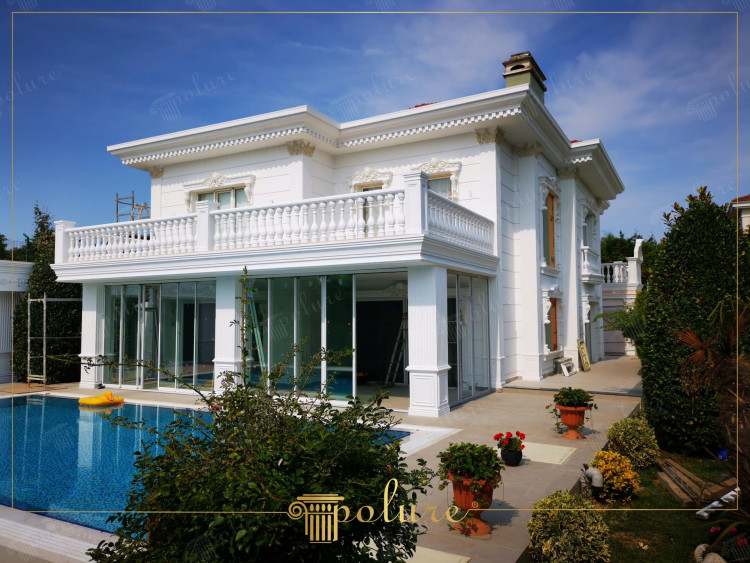 Poliuretanowe zdobienia w klasycznej willi z nowoczesnym akcentem <h2>Połączenie klasyki i nowoczesności</h2><p>Projekt tej willi łączy <strong>klasyczną architekturę</strong> z subtelnymi współczesnymi rozwiązaniami. Dekoracyjne gzymsy i balustrady z <strong>poliuretanu</strong> nadają elewacji elegancki rys, a jednocześnie zapewniają odporność na działanie warunków atmosferycznych. Biała kolorystyka fasady podkreśla czystość formy i kontrastuje z otoczeniem pełnym bujnej zieleni.</p><h2>Detal architektoniczny</h2><p>Widoczne są bogato zdobione pilastry oraz geometryczne układy zdobień, które nawiązują do antycznych tradycji porządków jońskich i korynckich. Subtelne ornamenty i powtarzalne rytmy kompozycji sprawiają, że fasada zyskuje głębię i wyrazistość. Balustrady na tarasie wprowadzają dodatkową warstwę dekoracyjności, tworząc elegancką linię poziomą nad parterem.</p><h2>Ogród i otoczenie</h2><p>Przestrzeń wokół willi została przemyślanie ukształtowana. Basen odbija kontury budynku i nadaje przestrzeni luksusowego charakteru. Donice z kwiatami oraz starannie przycięte krzewy wzbogacają kompozycję o kolory i tekstury, które harmonizują z imponującą fasadą.</p><h2>Krótka nota historyczna</h2><p>Dekoracyjne kolumny i balustrady, inspirowane wzorami antycznych willi śródziemnomorskich, mają korzenie sięgające tradycji architektury z czasów starożytnej Grecji i Rzymu. Tutaj zostały one odświeżone nowoczesnymi materiałami i proporcjami.</p>

<p>Ta willa prezentuje wyjątkowe połączenie klasyki i współczesności. Fasada ozdobiona jest gzymsami i balustradami wykonanymi z <strong>poliuretanu</strong>. Kolumny i pilastry nadają bryle monumentalny charakter. Białe powierzchnie podkreślają prostotę oraz szlachetność form. Transparentne przeszklenia nadają kompozycji lekkości. Ogród wypełniony jest bujną zielenią i geometrycznym układem roślin. Basen tworzy klimatyczny kontrast z klasyczną architekturą. Motywy inspirowane antykiem wprowadzają historyczny akcent. Nowoczesne detale wzmacniają funkcjonalność przestrzeni. Elewacja zyskuje elegancję dzięki ornamentalnym rytmom. Balustrady dopełniają symetrię układu. Światło i refleksy podkreślają dynamikę architektury. Zastosowane proporcje zachowują klasyczny balans. Projekt łączy <strong>tradycję</strong> i <strong>innowację</strong>. Całość ukazuje harmonię <strong>detali</strong> i nowoczesnej estetyki. Willa stanowi ponadczasowy przykład elegancji.</p>