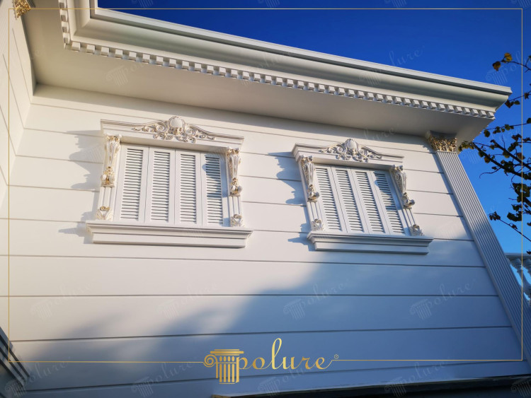 Poliuretan klasične fasadne i dekorativne sove za elegantne vile <h2>Klasična dekoracija fasade poliuretanskim elementima</h2><p>Upotreba <strong>poliuretanskih</strong> detalja u fasadnim rešenjima omogućava postizanje bogatih dekorativnih efekata bez kompromisa u trajnosti. Prozorski okviri su ukrašeni snažno oblikovanim <strong>ornamentima</strong> koji uključuju simetrične volute, geometrijske trake i akcentovane floralne motive u diskretnoj zlatnoj boji. Ovi detalji naglašavaju arhitektonsku eleganciju objekta i stvaraju skladan vizuelni ritam.</p><p>Horizontalne linije fasade daju preciznu geometriju, dok se u gornjem delu pojavljuje klasikizovani <strong>friz</strong> sastavljen od ponavljajućih trouglastih elemenata. Ovaj motiv potiče iz antičke tradicije gde je friz imao i konstruktivnu i simboličku ulogu. Kombinacija istorijskih uzora i savremenih materijala podseća na trajnu privlačnost klasičnog stila.</p><p>Prozorske roletne su uparene sa ukrasnim konzolama koje unose dodatnu vertikalnu dinamiku. Lagana belina površina kontrastira zlatnim akcentima na konzolama i kutovima, čime nastaje sofisticiran vizuelni balans.</p><ul><li>Otpornost poliuretana na vlagu i vremenske uticaje</li><li>Lagana montaža i fleksibilnost materijala</li><li>Mogućnost bogate <strong>dekoracije</strong> bez težine kamena</li><li>Dugovečnost i minimalno održavanje</li></ul><p>Ovakav pristup čini fasadu ne samo estetski dojmljivom, već i funkcionalno postojanom, nadovezujući se na tradiciju <strong>klasične arhitekture</strong> dok se uklapa u savremene potrebe.</p>
<p>Poliuretan omogućava izuzetnu preciznost u oblikovanju klasičnih fasadnih detalja. Prozori sa bogatim okvirima oživljavaju tradiciju aristokratskih vila. Dekorativne konzole u kombinaciji sa reljefnim motivima stvaraju dinamičan ritam. Horizontalne linije fasade obezbeđuju čist i elegantan profil. Gornji venac sa trouglastim frizom unosi osećaj istorijske dubine. Diskretni zlatni akcenti naglašavaju raskoš u detaljima. Bele površine stvaraju kontrast koji deluje profinjeno i luksuzno. Poliuretan kao materijal pruža trajnost i otpornost. Lakoća konstrukcije olakšava montažu i održavanje. Ukrasne <strong>ornamente</strong> moguće je prilagoditi različitim stilovima. Kombinacija geometrije i floralnih linija daje fasadi skladan karakter. Inspiracija klasičnom arhitekturom povezuje prošlost i sadašnjost. Elegancija prozorskih ramova naglašava vertikalni sklad. Čitav dizajn unosi harmoničnu estetsku ravnotežu. Ovakvo rešenje spaja <strong>dekoraciju</strong>, funkcionalnost i trajnu lepotu.</p>