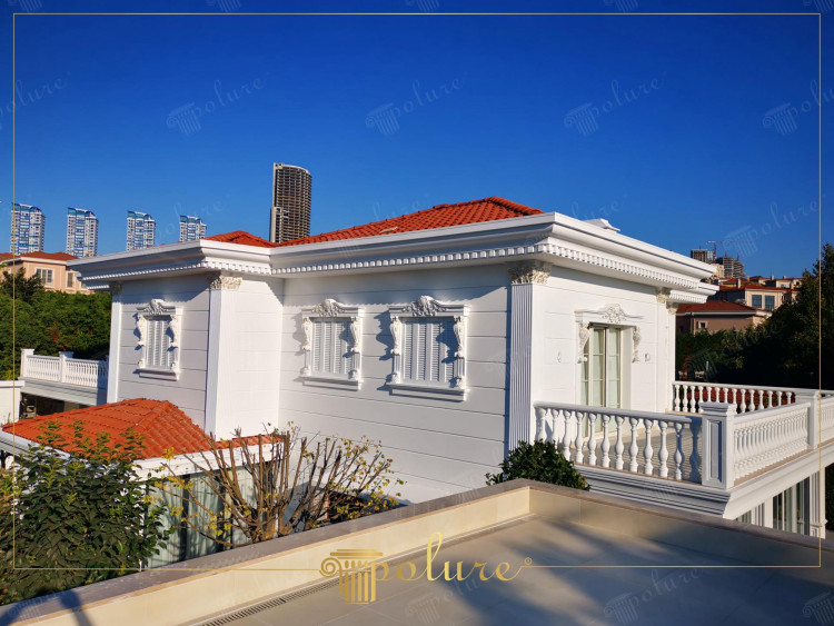 Elewacja willi z klasycznymi detalami poliuretanowymi i czerwonym dachem <h2>Klasyczne piękno poliuretanowej elewacji</h2><p>Willa prezentuje elegancję, w której biała fasada zestawia się z mocnym akcentem czerwonego dachu z dachówki. Na elewacji dominują <strong>poliuretanowe</strong> gzymsy, pilastry i zdobienia wokół okien, które nadają całości monumentalny wygląd znany z architektury klasycznej.</p><p>Bogate detale dekoracyjne takie jak <strong>ornamenty</strong> roślinne, festony i geometryczne ramki wokół okien wzmacniają rytm oraz harmonię budynku. Balustrady balkonowe złożone z symetrycznych tralek nadają mu wrażenie lekkości i są charakterystycznym elementem stylu rezydencjonalnego.</p><p>Poliuretan, jako materiał współczesny, oferuje lekkość i trwałość przy jednoczesnym zachowaniu efektu inspirowanego kamieniem. Dzięki temu można odtworzyć bogactwo dawnych detali, unikając ciężaru i kosztów tradycyjnego kamienia.</p><p>W krótkiej perspektywie historycznej można zauważyć, że podobne formy dekoracyjne były używane w architekturze klasycyzmu i renesansu, gdzie kolumny oraz gzymsy podkreślały rangę budynku.</p><ul><li>Wyrazista gra kontrastu czerwonego dachu i białej fasady</li><li><strong>Detale architektoniczne</strong> inspirowane klasycznymi porządkami</li><li>Balustrady tworzące rytm oraz elegancję fasady</li><li>Odporne na warunki atmosferyczne <strong>elementy dekoracyjne</strong></li></ul>

<p>Elegancka willa zyskała unikalny charakter dzięki zastosowaniu białej fasady i kontrastu z czerwonym dachem. Dekoracyjne gzymsy podkreślają monumentalność bryły. Bogato zdobione obramienia okien nadają rytm elewacji. Balustrady w klasycznym stylu wzmacniają estetykę całości. Poliuretanowe detale zachowują wygląd tradycyjnego kamienia. Ich lekkość i trwałość ułatwiają realizację. Zastosowane <strong>ornamenty</strong> roślinne budują nastrój elegancji. Geometryczne akcenty dodają symetrii. Zestawienie kolorów tworzy efekt luksusu. <strong>Elewacja</strong> wyróżnia się ponadczasową formą. Inspiracje renesansowe są widoczne w proporcjach i detalach. Historia klasycyzmu przypomina o roli kolumn i gzymsów. Materiał <strong>poliuretan</strong> pozwala zachować autentyczny wygląd. Wnętrze willi zyskuje prestiż dzięki fasadzie. Całość wpisuje się w trend klasycznych willi miejskich.</p>