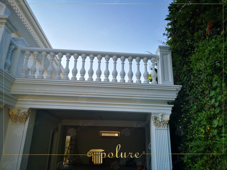Villa classica con dettagli in poliuretano e balcone con balaustre <h2>Eleganza delle balaustre classiche</h2><p>Il balcone con <strong>balaustre</strong> scolpite rappresenta un elemento distintivo del design della villa. Le forme sinuose e proporzionate creano un ritmo architettonico che trae ispirazione dalle residenze aristocratiche europee. La disposizione regolare degli elementi verticali garantisce solidità visiva ed equilibrio estetico.</p><h2>Colonne e capitelli decorati</h2><p>Le colonne scanalate con capitelli arricchiti da dettagli dorati richiamano lo stile <strong>corinzio</strong>, molto diffuso nell’antica Grecia e ripreso nell’architettura rinascimentale. La presenza di fogliami stilizzati e volute dorate aggiunge valore decorativo e richiama la tradizione della bellezza classica.</p><h2>Geometria e proporzioni</h2><p>I profili orizzontali, con cornici sovrapposte e fregi lineari, enfatizzano la proporzione e la <strong>simmetria</strong>. Questo gioco di rientranze e sporgenze non solo conferisce profondità, ma produce un impatto scenico notevole sulla facciata esterna.</p><h2>Armonia cromatica</h2><p>Il <strong>bianco</strong> luminoso della superficie principale contrasta con le finiture dorate dei capitelli, creando un effetto raffinato. Questo abbinamento cromatico è tipico delle ville classiche, dove la chiarezza dei volumi si unisce al lusso discreto dei dettagli metallici.</p><h2>Rilevanza storica</h2><p>L’uso di colonne e capitelli decorati risale all’antica Roma e alla Grecia, dove la <strong>architettura</strong> classica stabiliva canoni di proporzione e bellezza destinati a influenzare i secoli successivi. Questa villa riprende quegli elementi adattandoli a un linguaggio moderno attraverso l’impiego del <strong>poliuretano</strong>, materiale leggero e resistente.</p>
<p>La villa con dettagli in <strong>poliuretano</strong> esprime un’eleganza senza tempo. Il balcone con <strong>balaustre</strong> scolpite dona ritmo visivo alla facciata. Le colonne con capitelli dorati evidenziano ispirazioni dallo stile <strong>corinzio</strong>. Le proporzioni regolari trasmettono armonia architettonica. Le cornici geometriche sottolineano la solidità del design. Il colore <strong>bianco</strong> riflette la luce e valorizza i volumi. I dettagli dorati impreziosiscono l’aspetto complessivo. Le superfici pulite mantengono un carattere raffinato. L’uso del <strong>poliuretano</strong> garantisce durata e leggerezza. Le decorazioni fogliate richiamano un’estetica classica. La simmetria delle balaustre rafforza l’equilibrio visivo. La tradizione storica si fonde con tecniche moderne. La raffinatezza emerge in ogni dettaglio della facciata. L’abbinamento cromatico accentua il lusso discreto. L’insieme offre un modello ideale di architettura classica contemporanea.</p>