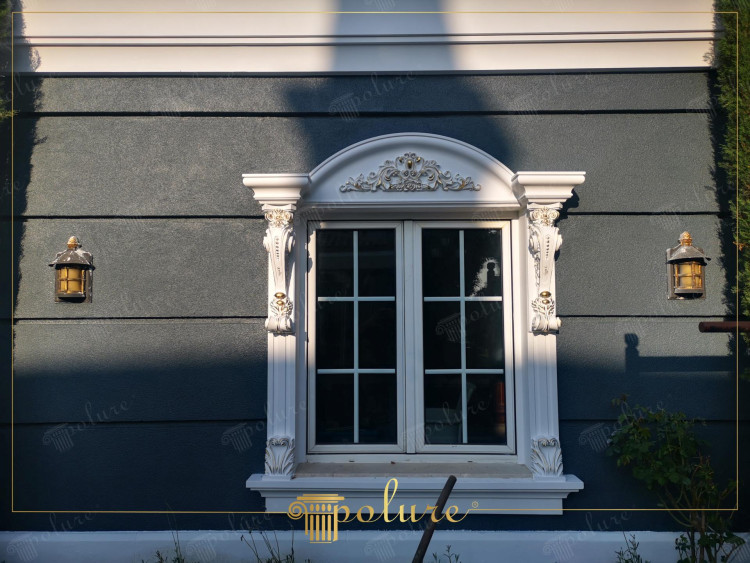 Klasyczne zdobienia poliuretanowe wokół eleganckiego okna fasadowego <h2>Elegancka fasada z dekoracyjnymi detalami</h2><p>Projekt okna wykorzystuje <strong>poliuretan</strong> jako główny materiał zdobniczy, co pozwala na precyzyjne odwzorowanie klasycznych motywów. Struktura ramy wyróżnia się symetrycznymi kolumnami, ozdobionymi <strong>ornamentami</strong> roślinnymi, w tym liśćmi akantu i spiralnymi motywami inspirowanymi sztuką antyczną.</p><p>Centralna część zwieńczona jest łukiem, w którym umieszczono <strong>dekoracyjny gzyms</strong> z roślinną kompozycją o subtelnym reliefie. Kontrast pomiędzy białymi zdobieniami a ciemnoszarą teksturą ściany tworzy elegancką kompozycję nadającą budynkowi wrażenie solidności i harmonii.</p><p>Z historycznego punktu widzenia tego rodzaju formy nawiązują do tradycji architektury renesansowej i barokowej, gdzie <strong>symetria</strong> i bogate zdobienia podkreślały prestiż posesji. Boczne kinkiety w klasycznym stylu uzupełniają całość, dodając funkcjonalne i estetyczne oświetlenie.</p><ul><li>Ramy z detalami akantowymi</li><li>Łukowate zwieńczenie z dekoracyjnym gzymsem</li><li>Boczna ornamentyka z kolumnami</li><li>Detale wykonane z trwałego poliuretanu</li></ul><p>Tego typu aranżacja jest przykładem, jak wykorzystanie precyzyjnie zdobionych elementów może nadać fasadzie zarówno elegancję, jak i ponadczasowy charakter.</p>

<p>Projekt fasady podkreśla znaczenie klasycznych detali w estetyce budynków. Okno obramowane jest bogatymi zdobieniami z <strong>poliuretanu</strong>. Zastosowany materiał zapewnia trwałość i odporność na warunki atmosferyczne. Zdobienia inspirowane są ornamentyką renesansową. Centralnym punktem kompozycji jest łuk z dekoracyjnym gzymsem. Pojawiają się tu motywy roślinne i spiralne wzory. Boczne kolumny z liśćmi akantu nadają architekturze lekkości. Wyraźny kontrast między bielą a ciemną fasadą wzmacnia efekt wizualny. Kinkiety umieszczone po bokach podkreślają symetrię. Całość prezentuje się harmonijnie i elegancko. Projekt nadaje budynkowi reprezentacyjny charakter. Inspiracje barokowe i klasycystyczne wzmacniają estetykę. Reliefy tworzą grę światła i cienia. Fasada staje się nie tylko ozdobą, ale i wizytówką domu. Takie klasyczne podejście do detalu świadczy o dbałości architekta.</p>